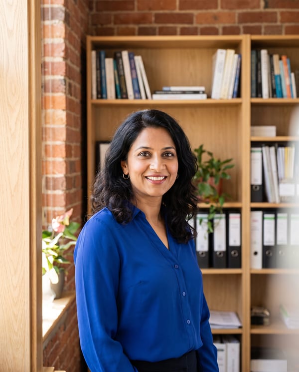 Hannah Mehta, tax preparer, in a royal blue blouse beside a bookshelf in the office